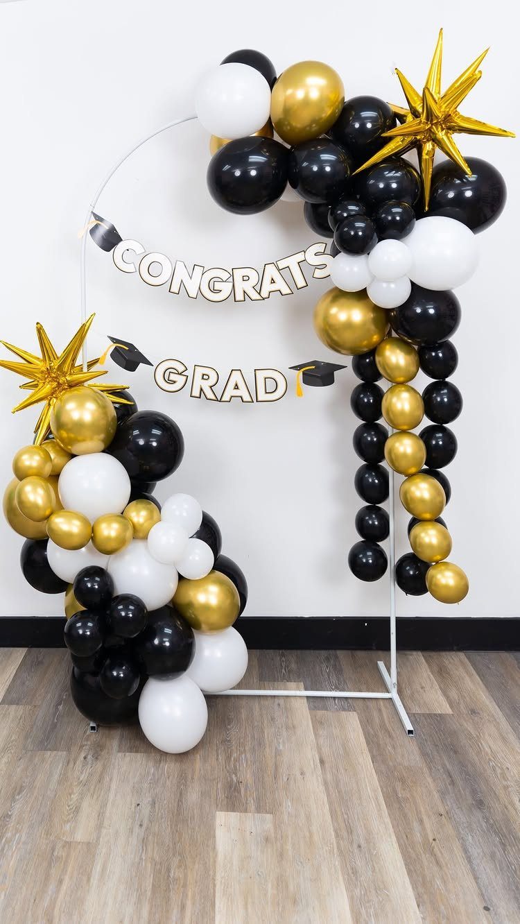 Graduation party decoration kit with black, gold, and white balloon garland on circular frame