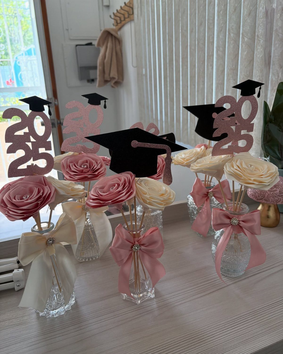 Graduation centerpieces with pink roses, 2025 glitter signs, and black graduation caps.