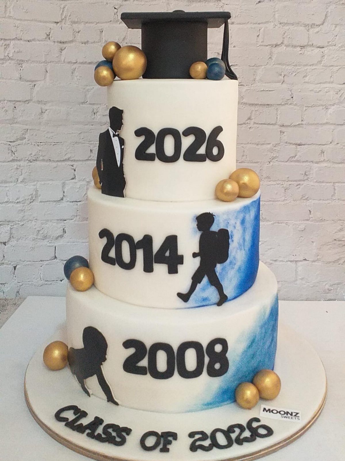 Three-tiered white graduation cake with student silhouettes, years, and a graduation cap topper.