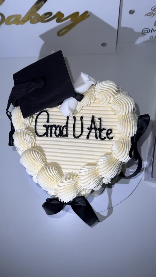 Heart-shaped white cake topped with a black graduation cap and 'Grad U Ate' text.
