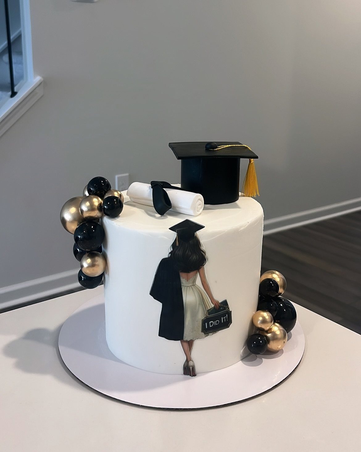 White graduation cake with a black cap, diploma, and graduate figure cutout.