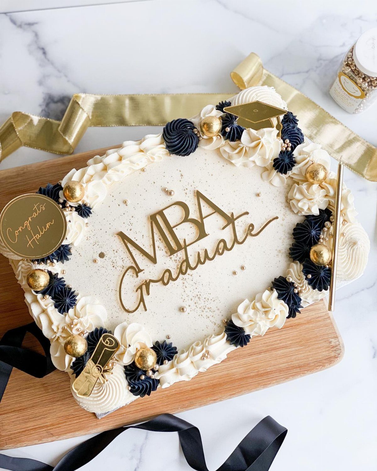 Rectangular white graduation cake with navy frosting, gold pearls, and MBA Graduate topper.