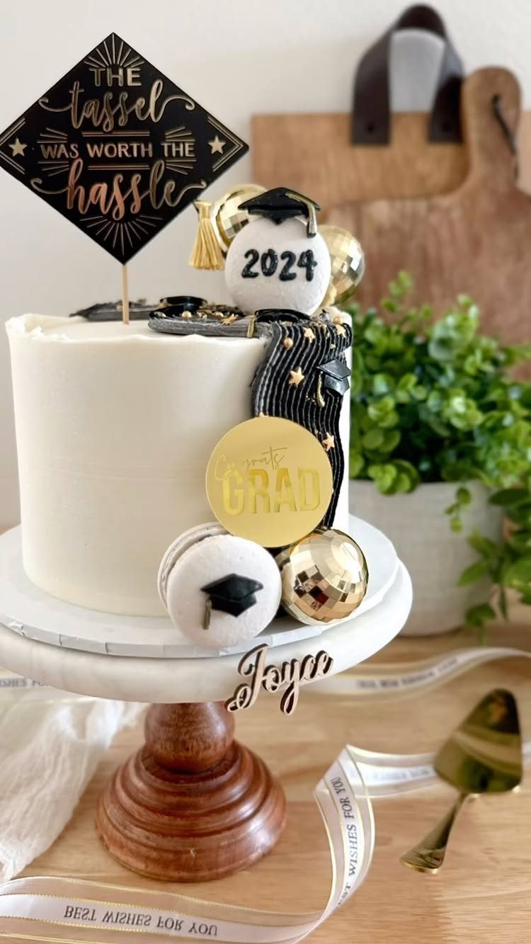 White graduation cake with gold accents, macarons, and a tassel themed topper.