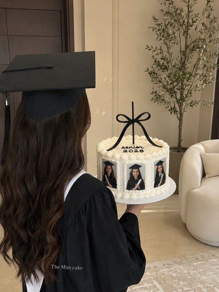 White graduation cake with edible photos of a graduate and a black bow topper.