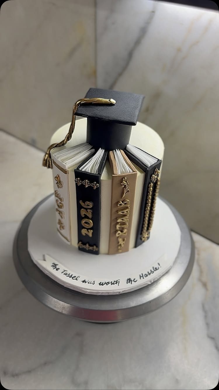 Graduation cake shaped like books topped with a black cap and gold tassel.