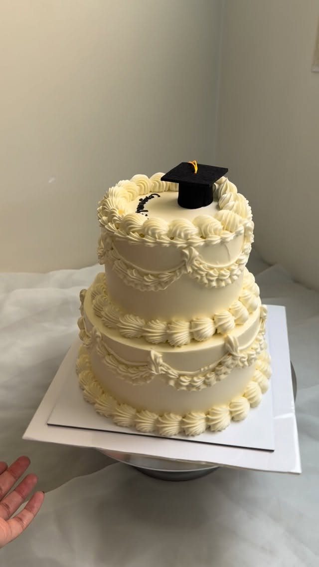 Two-tiered white frosted cake topped with a small black graduation cap and tassel.
