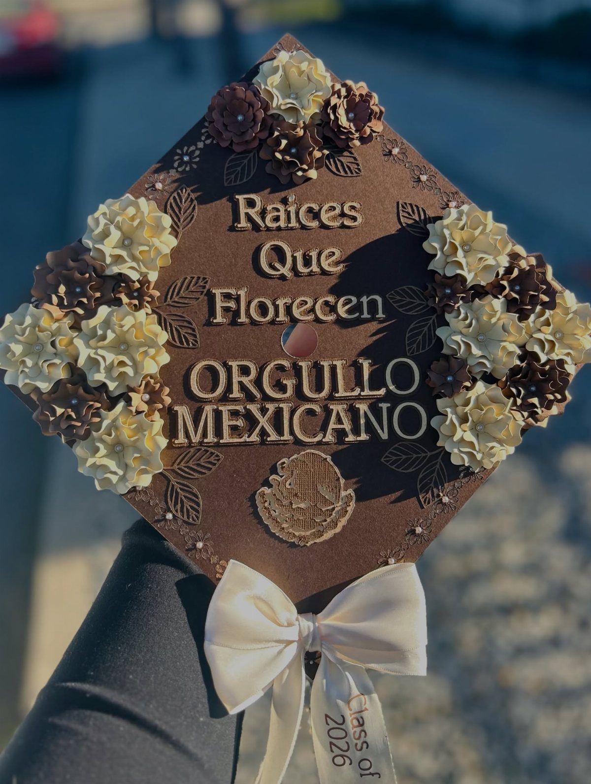 Decorated brown graduation cap with faux flowers and gold Mexican pride lettering.
