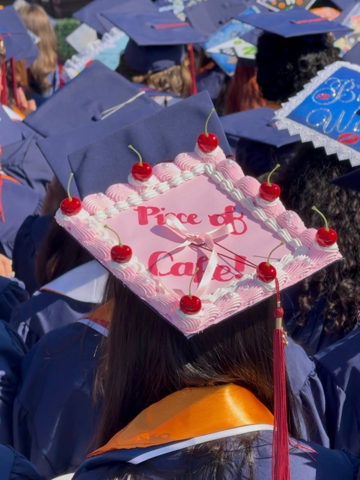 Graduation cap decorated as a pink cake with cherries and Piece of Cake text.