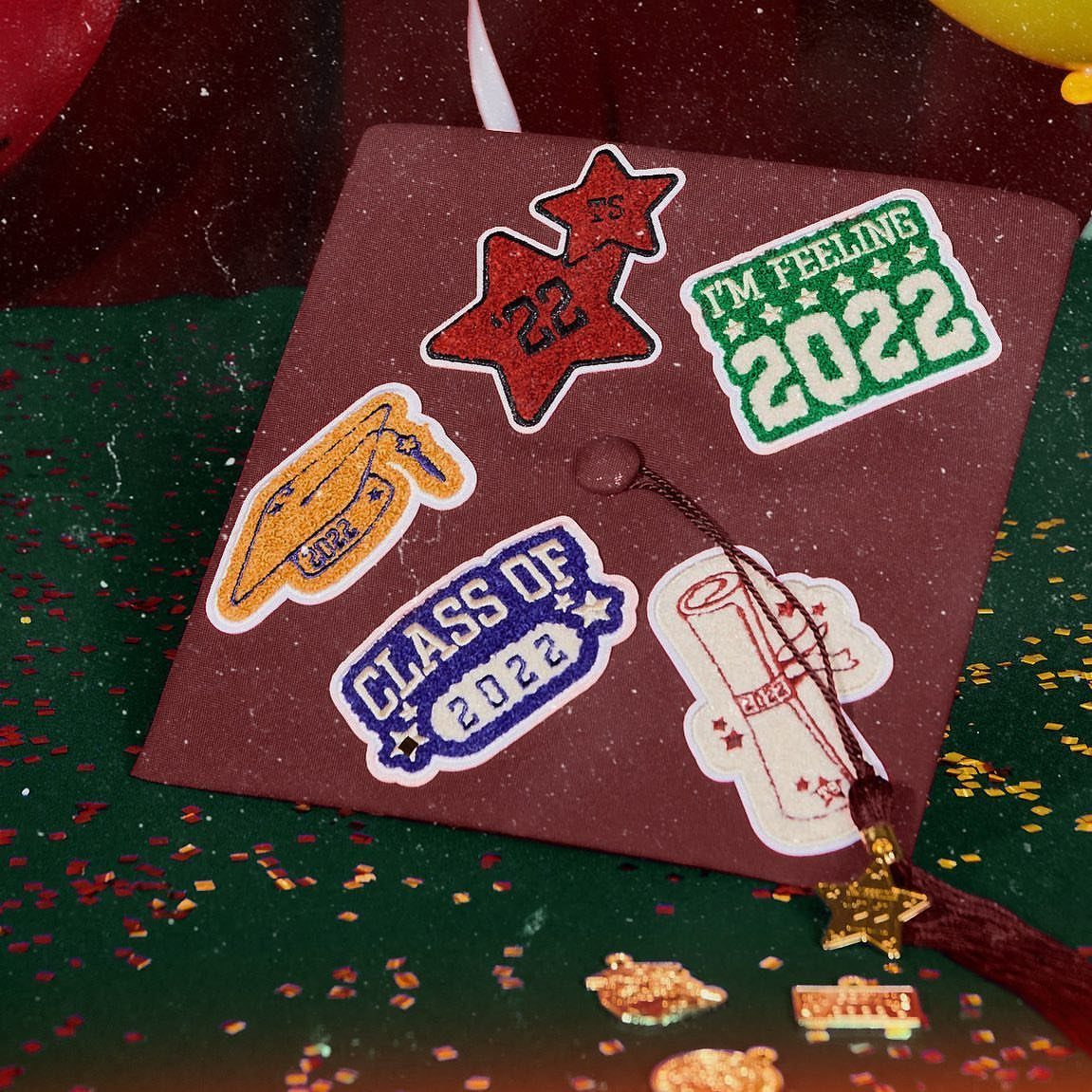 Maroon graduation cap with glittery 2022 stickers on a sparkling green background
