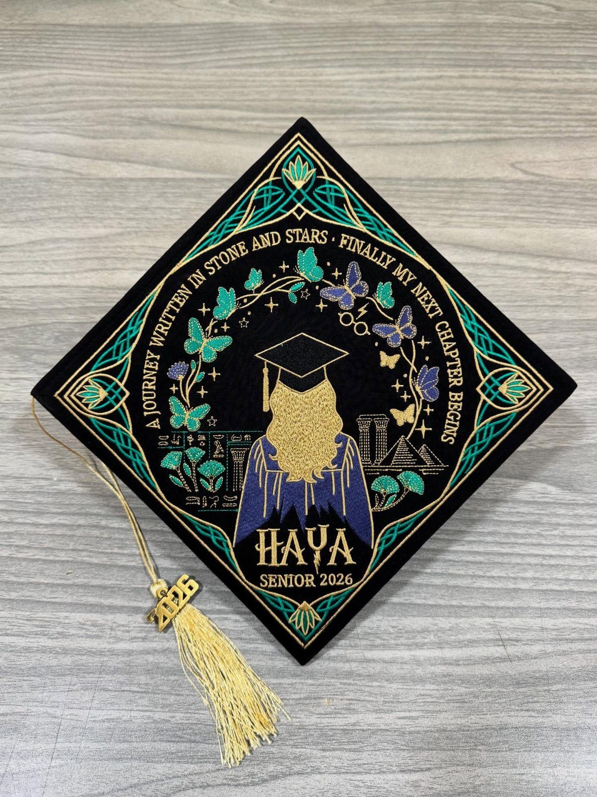 Decorated graduation cap with gold text and blue and green artistic illustrations.