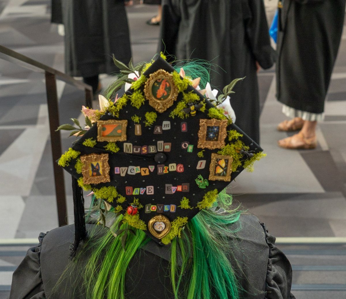 Decorated graduation cap with green moss, miniature gold frames, and sentimental text.