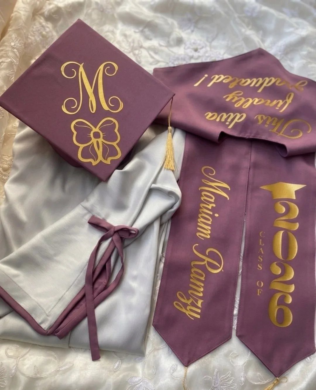 Purple graduation cap and stole with gold lettering next to a white gown.