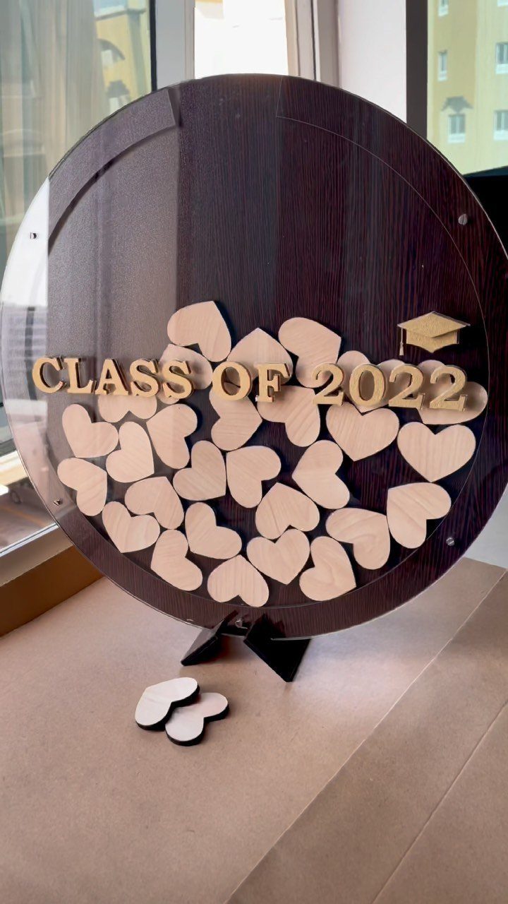 Circular wooden graduation guest book with gold text and small wooden heart tokens.