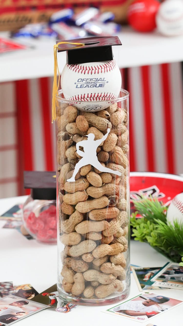 Baseball wearing a black graduation cap atop a glass jar filled with peanuts.