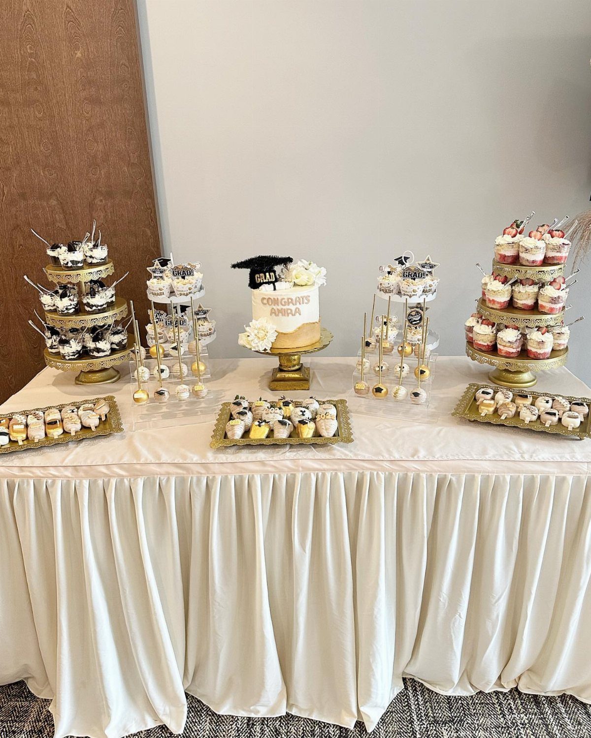 Tiered gold cupcake stands and a graduation cake on a white draped table.