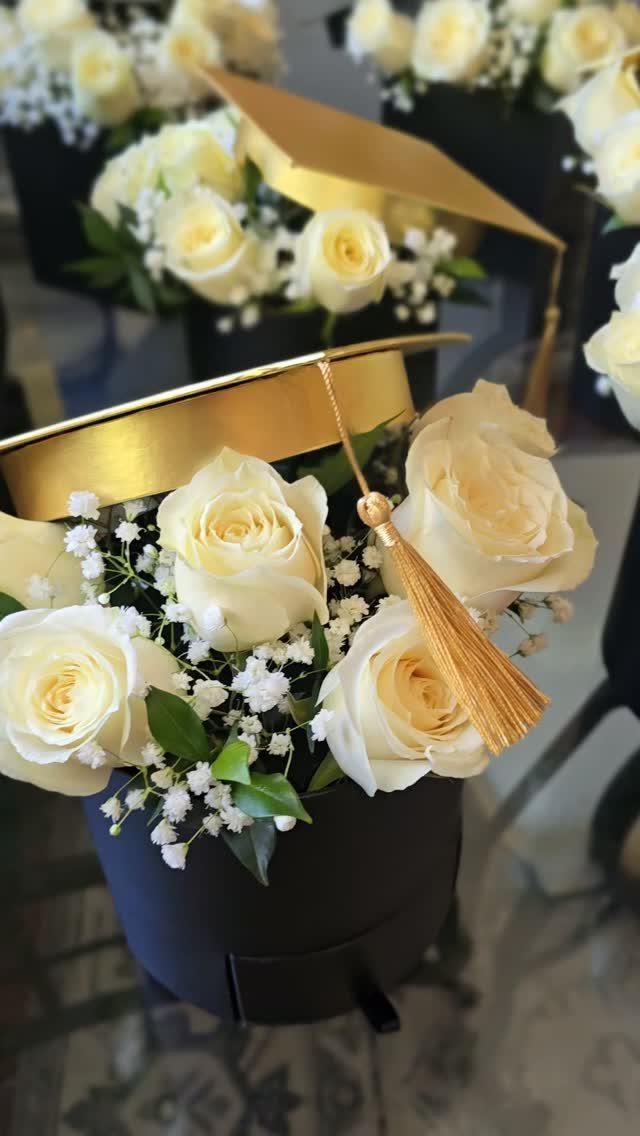 White roses in a black vase topped with a gold graduation cap centerpiece