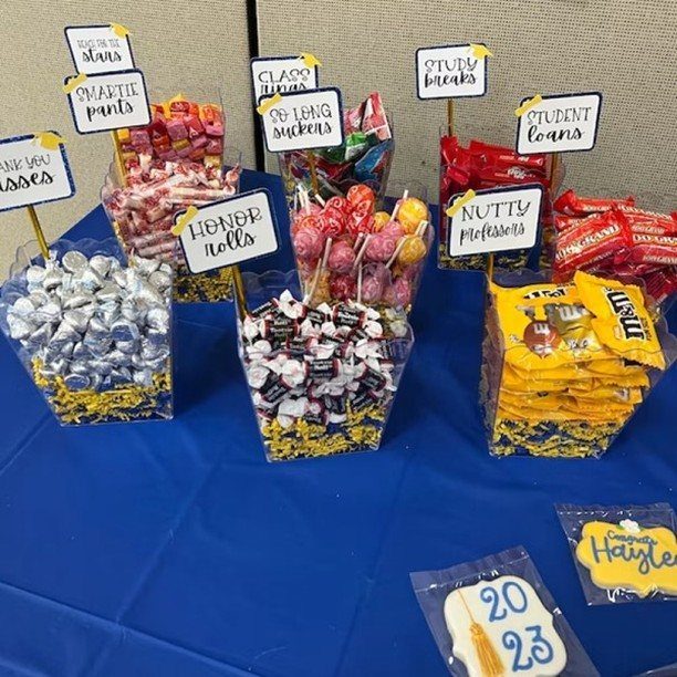 Candy centerpieces with graduation-themed puns on a blue table for a party.