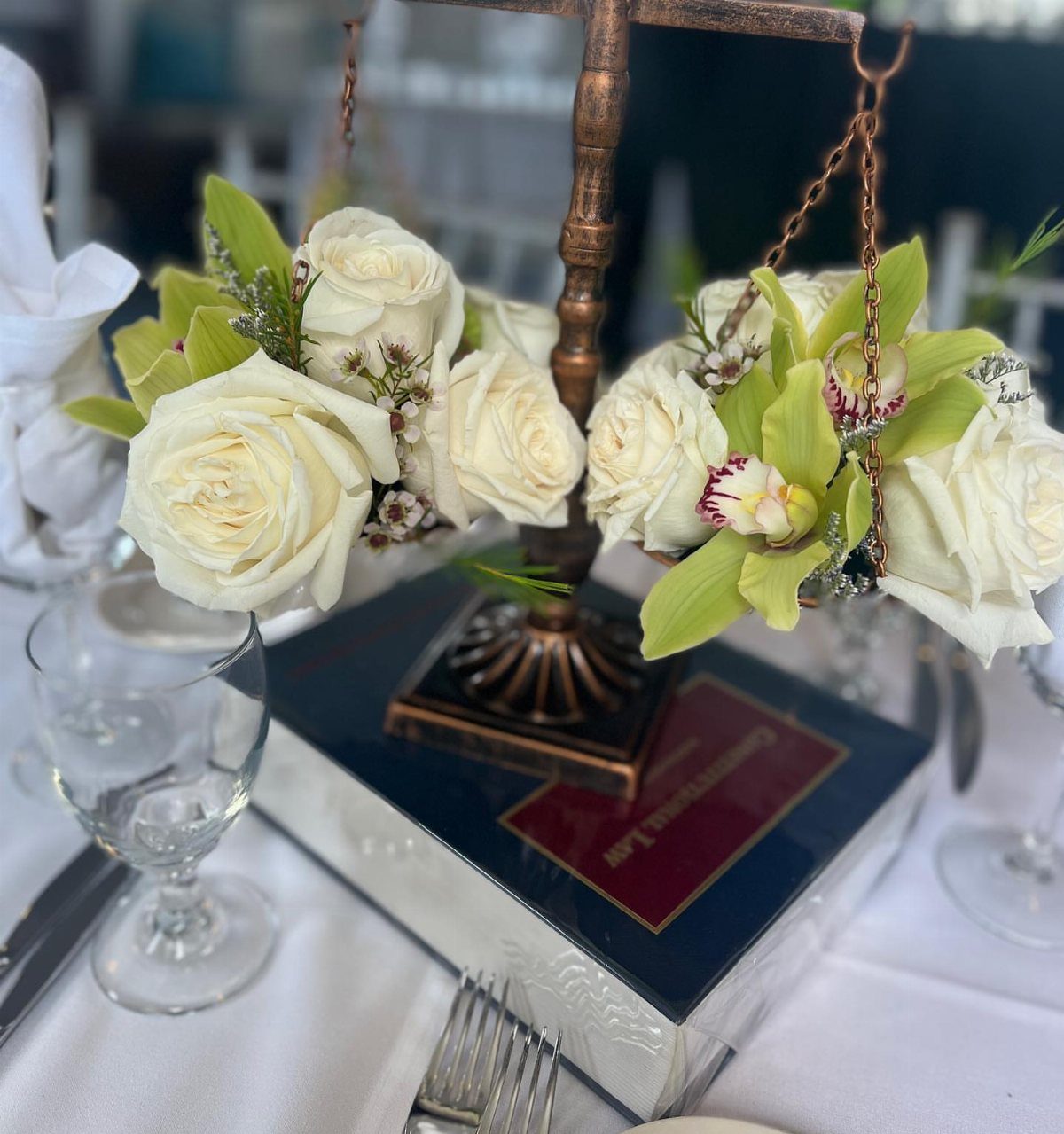Bronze scales of justice with white roses and orchids on a law book.