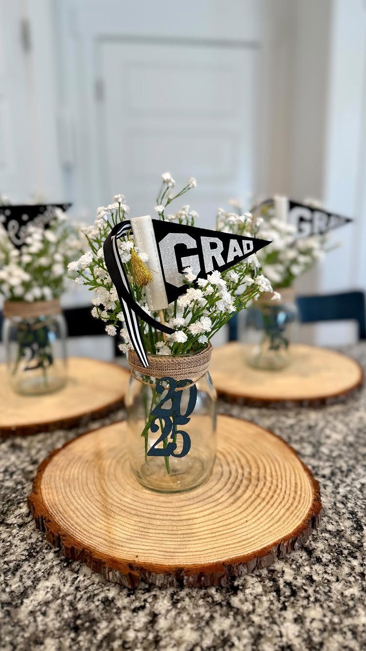 Mason jars with white flowers and graduation pennants on rustic wooden slice coasters.