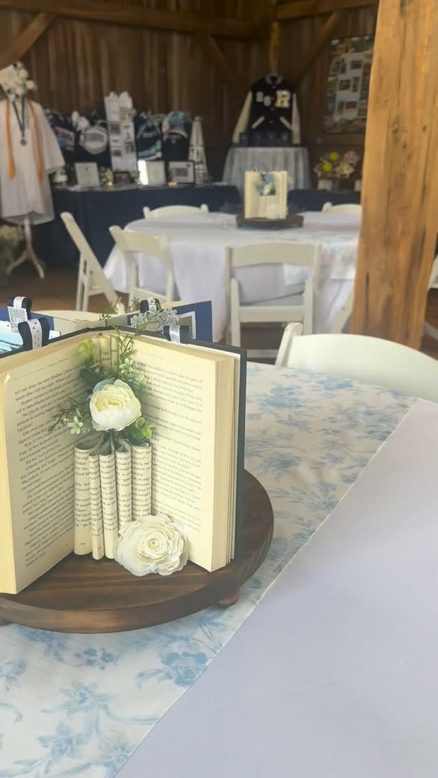 Open book centerpiece with white flowers and rolled pages on a wooden base