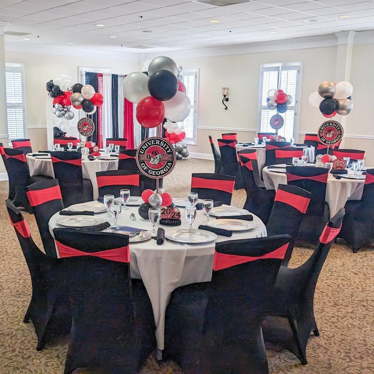 Graduation party tables with red, black, and silver balloon centerpieces and university logos.