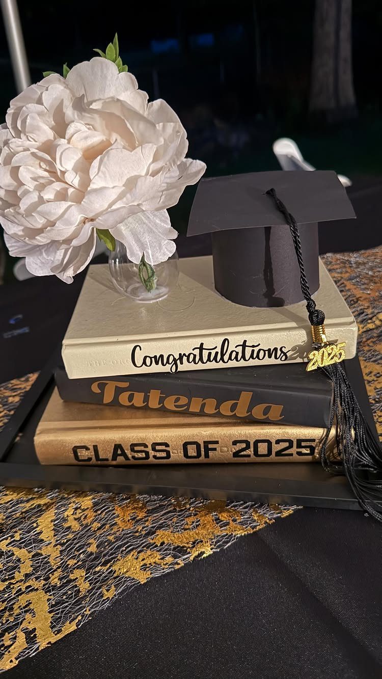 Graduation centerpiece with stacked books, a black mortarboard cap, and a white peony.