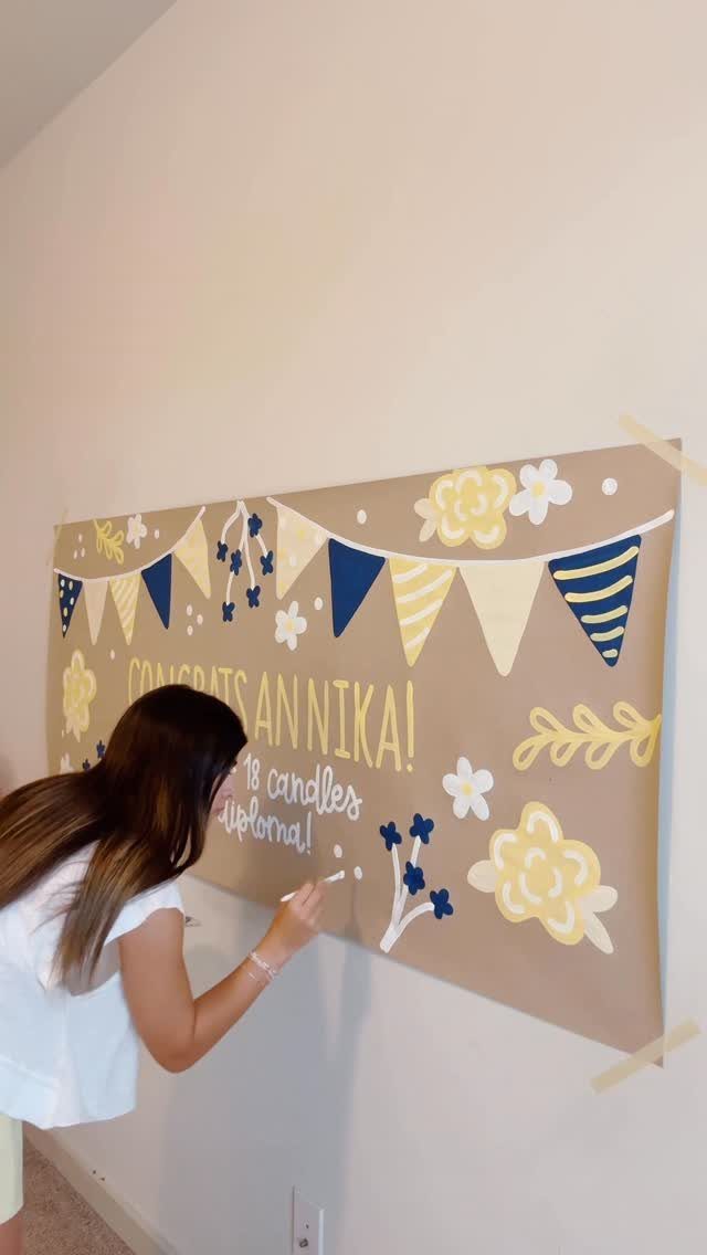Woman painting a brown craft paper banner with blue and yellow decorations on wall