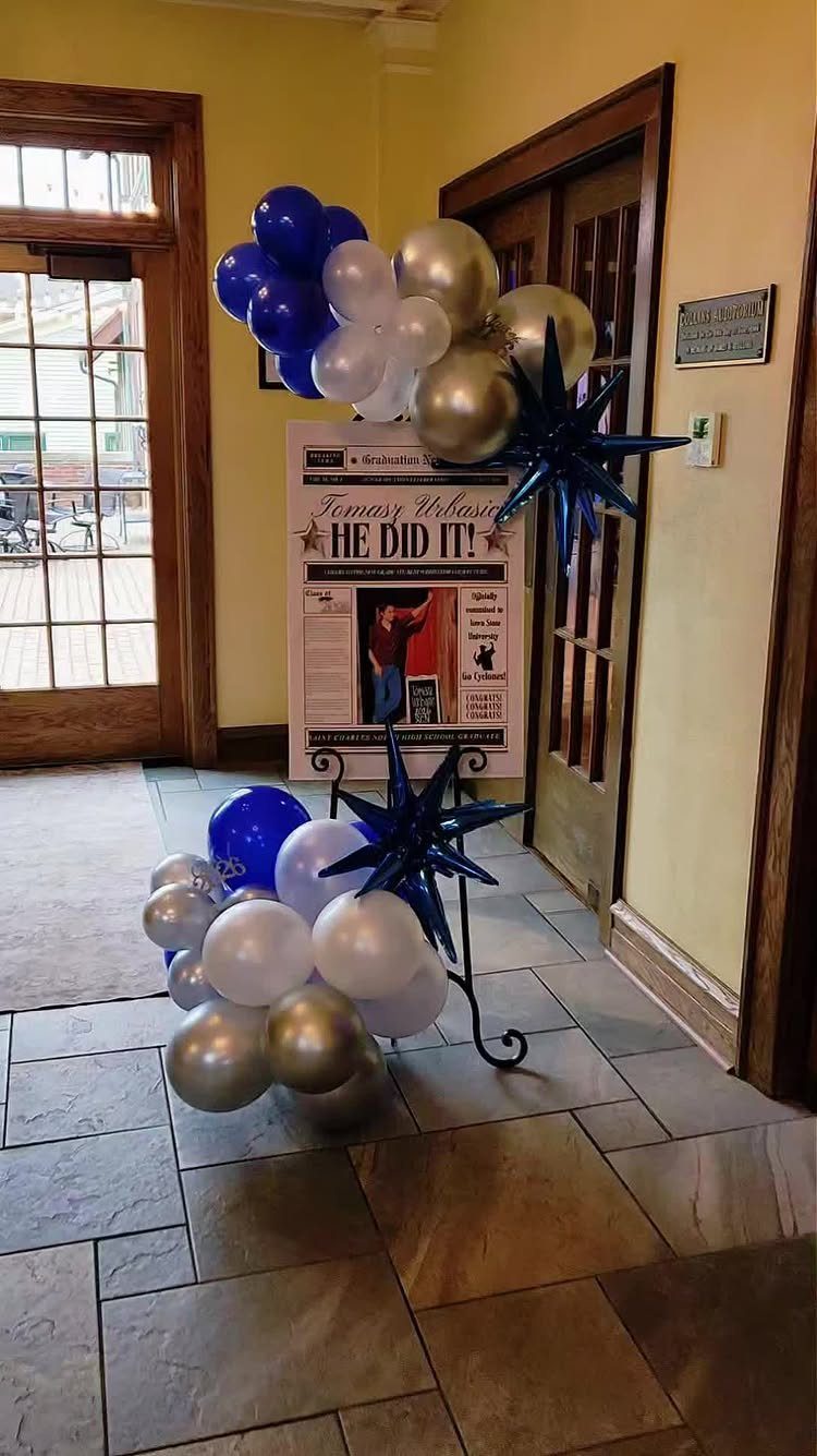 Graduation display with blue, white, and gold balloons surrounding a custom newspaper sign.
