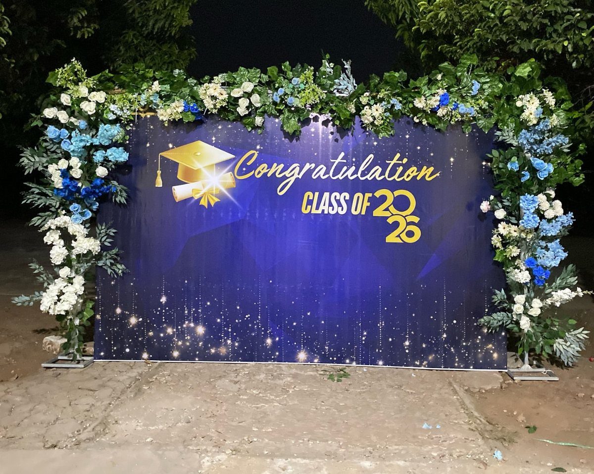 Blue graduation backdrop with gold text framed by white and blue floral arch.