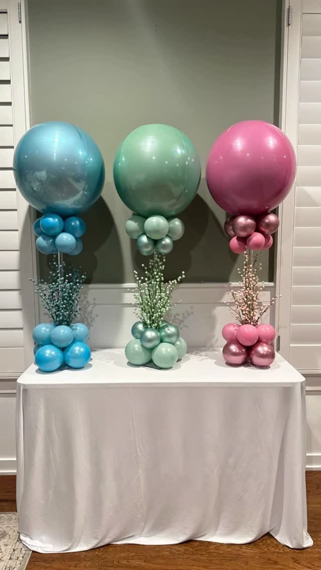 Three colorful balloon columns in blue, green, and pink on a white table.
