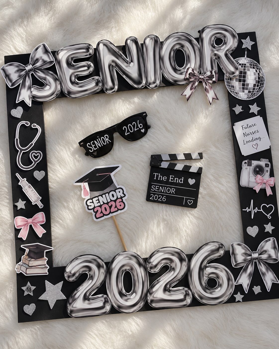 Black photo frame decorated with silver balloons and graduation props on white fur.