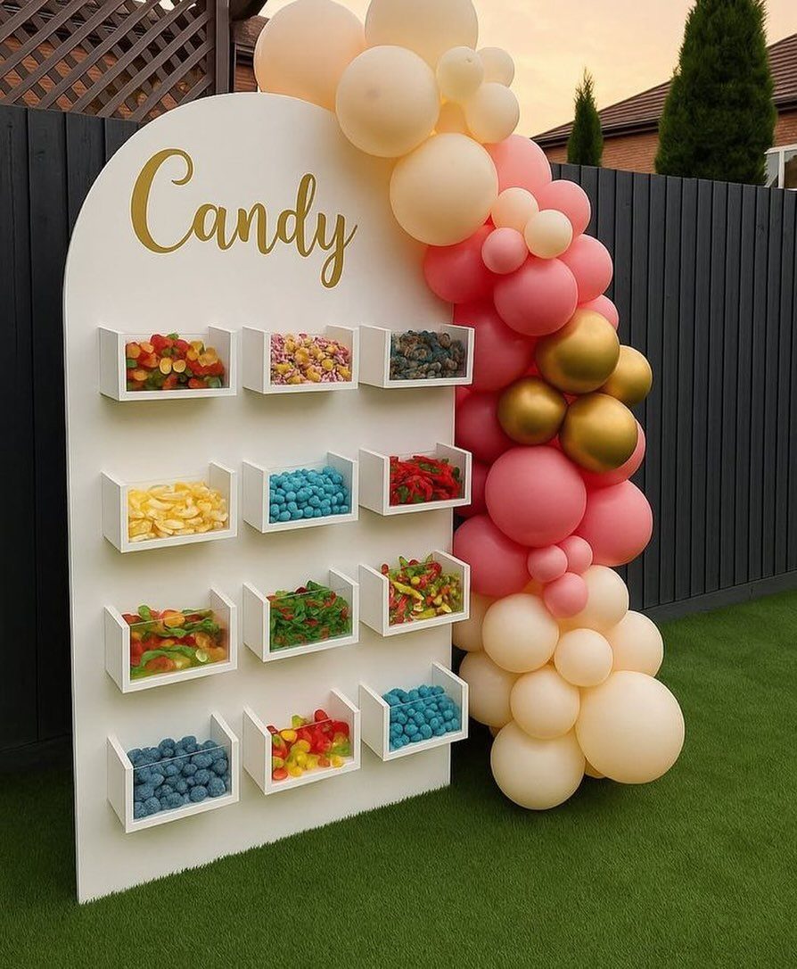 Candy wall with colorful sweets and a pink and gold balloon garland.