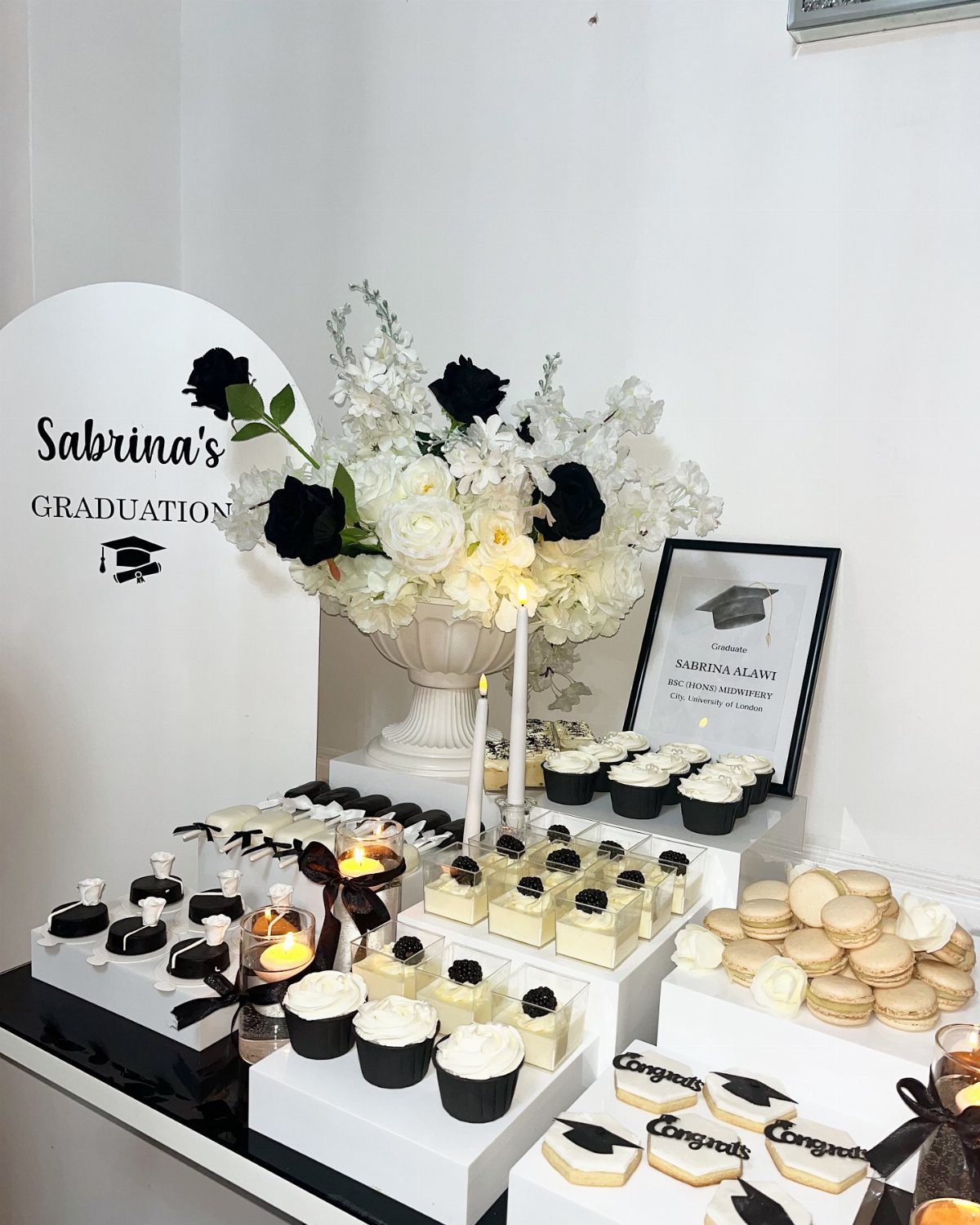 Graduation dessert table with black and white cupcakes, macarons, and floral centerpiece.