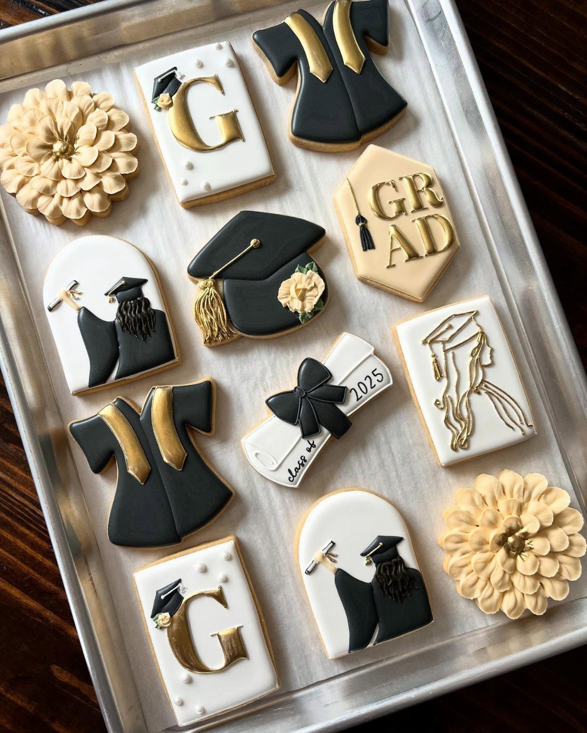 Graduation themed sugar cookies including a rolled diploma, caps, and gowns on a tray