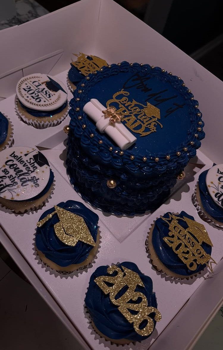 Blue graduation cake and cupcakes with gold toppers in a white box