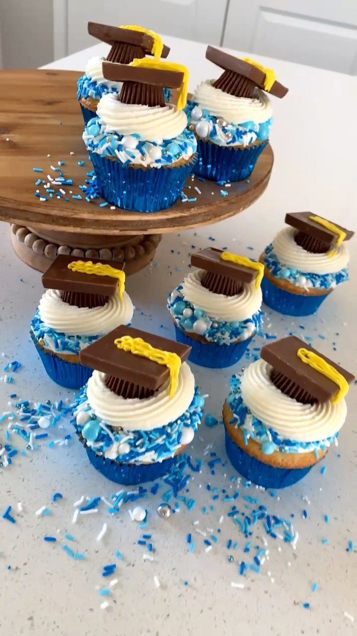 Graduation cap cupcakes with white frosting and blue sprinkles on a wooden stand.