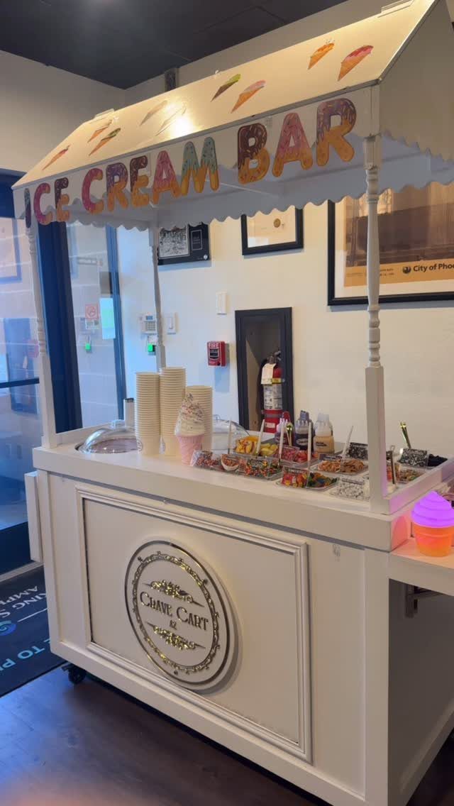 White ice cream cart with a cream awning and various toppings on counter