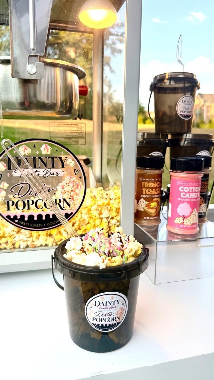 Popcorn machine and buckets of gourmet popcorn on a white table.