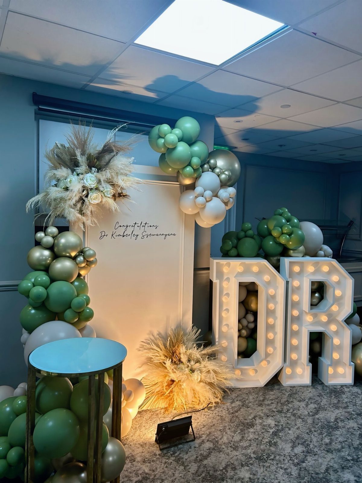 Party backdrop with green balloons and large illuminated DR letters for a doctor graduation.