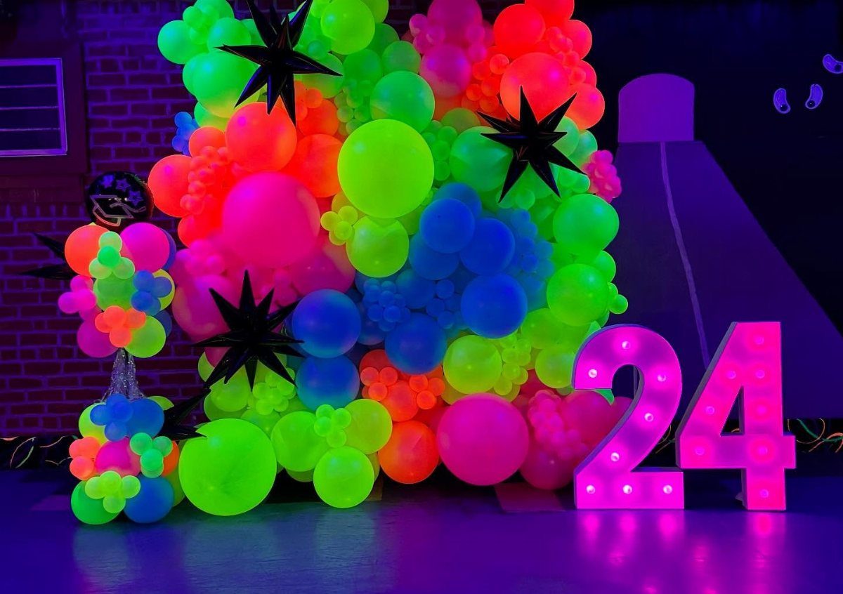 Neon colored balloon arch with black stars and glowing pink number 24.