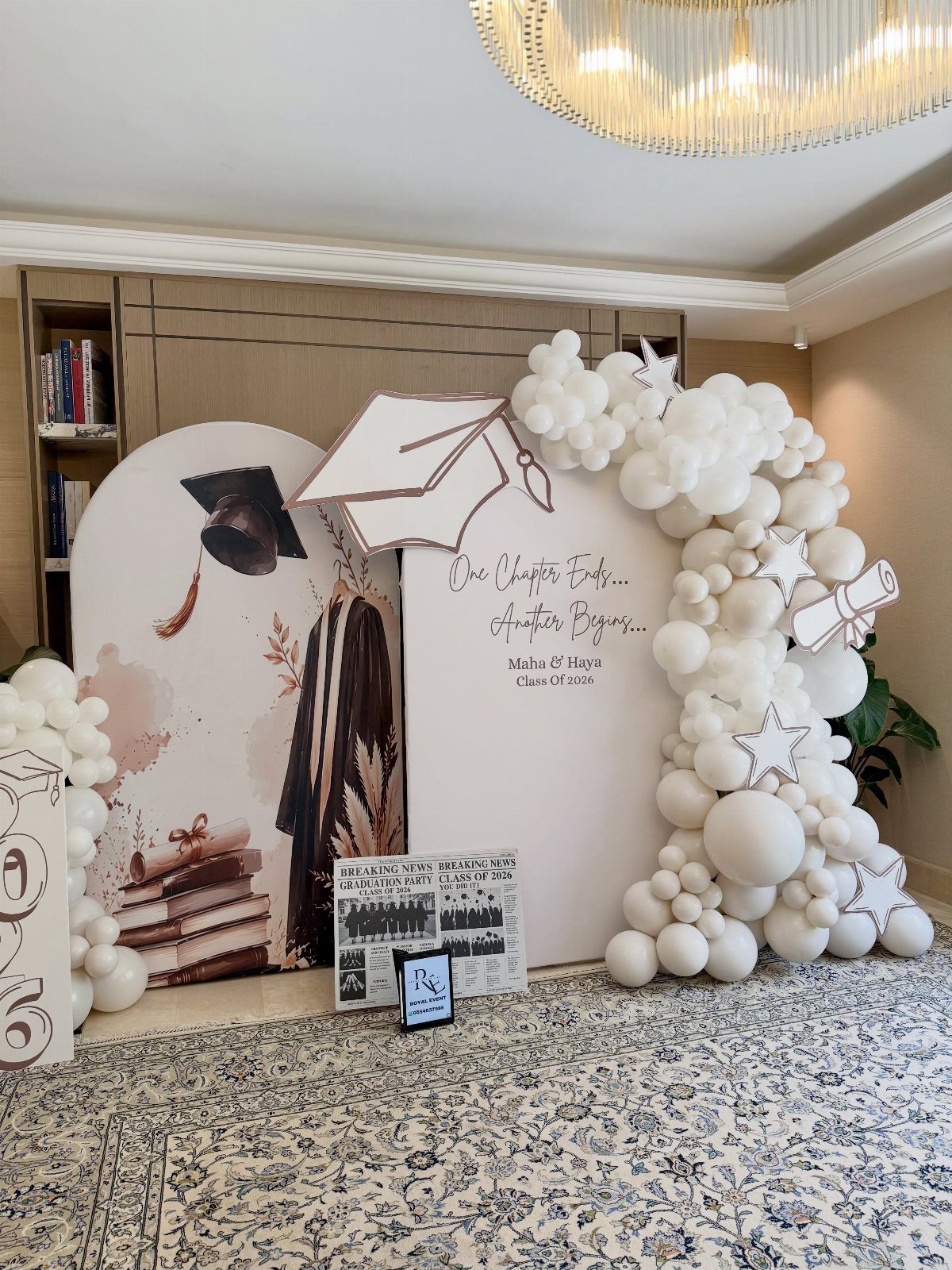 Graduation party backdrop with white balloon arch and graduation cap cutout decoration.