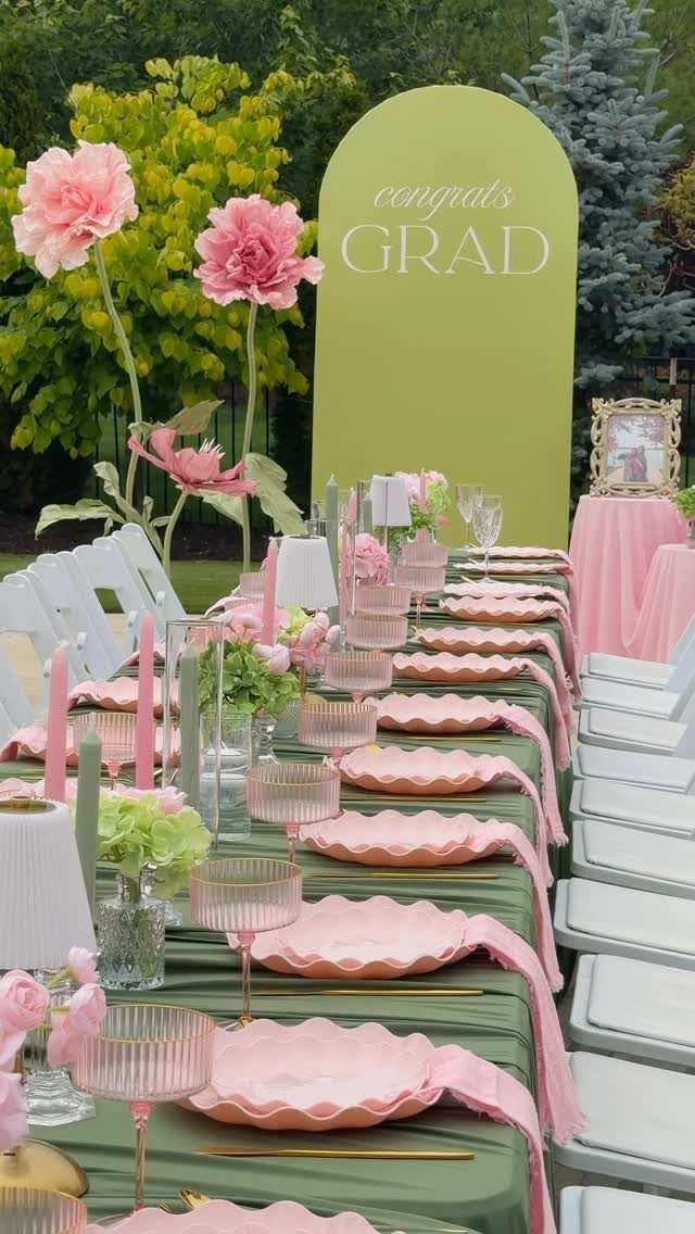 Outdoor graduation party table with pink plates and a congrats grad backdrop