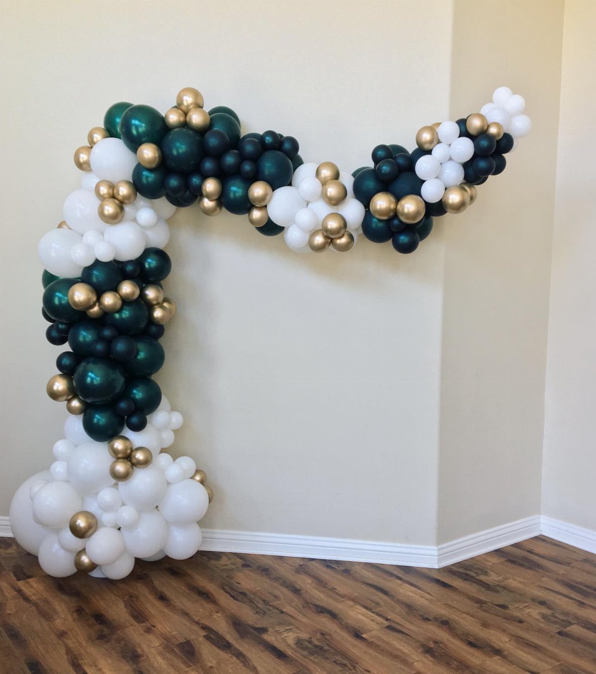Dark green, white, and gold balloon arch curving against a beige wall.