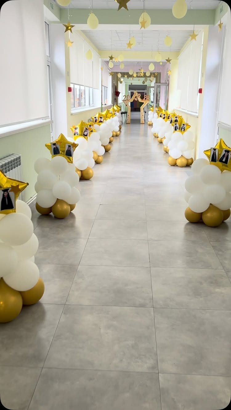 Hallway decorated with gold and white balloon clusters and hanging gold stars.