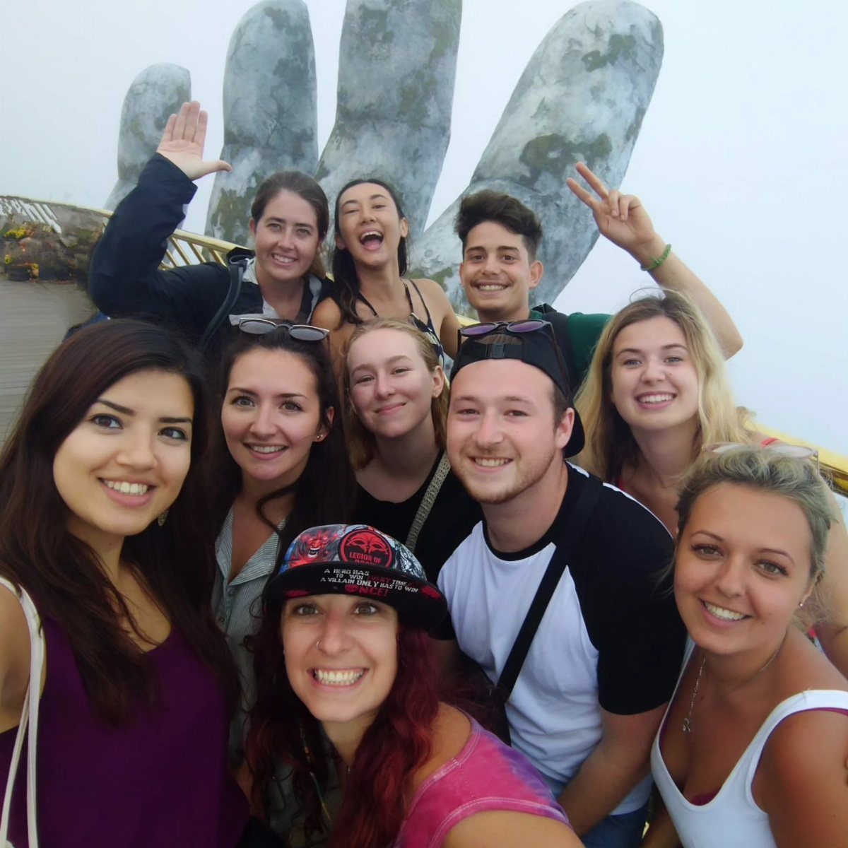 Group of young adults smiling in front of a giant stone hand sculpture.