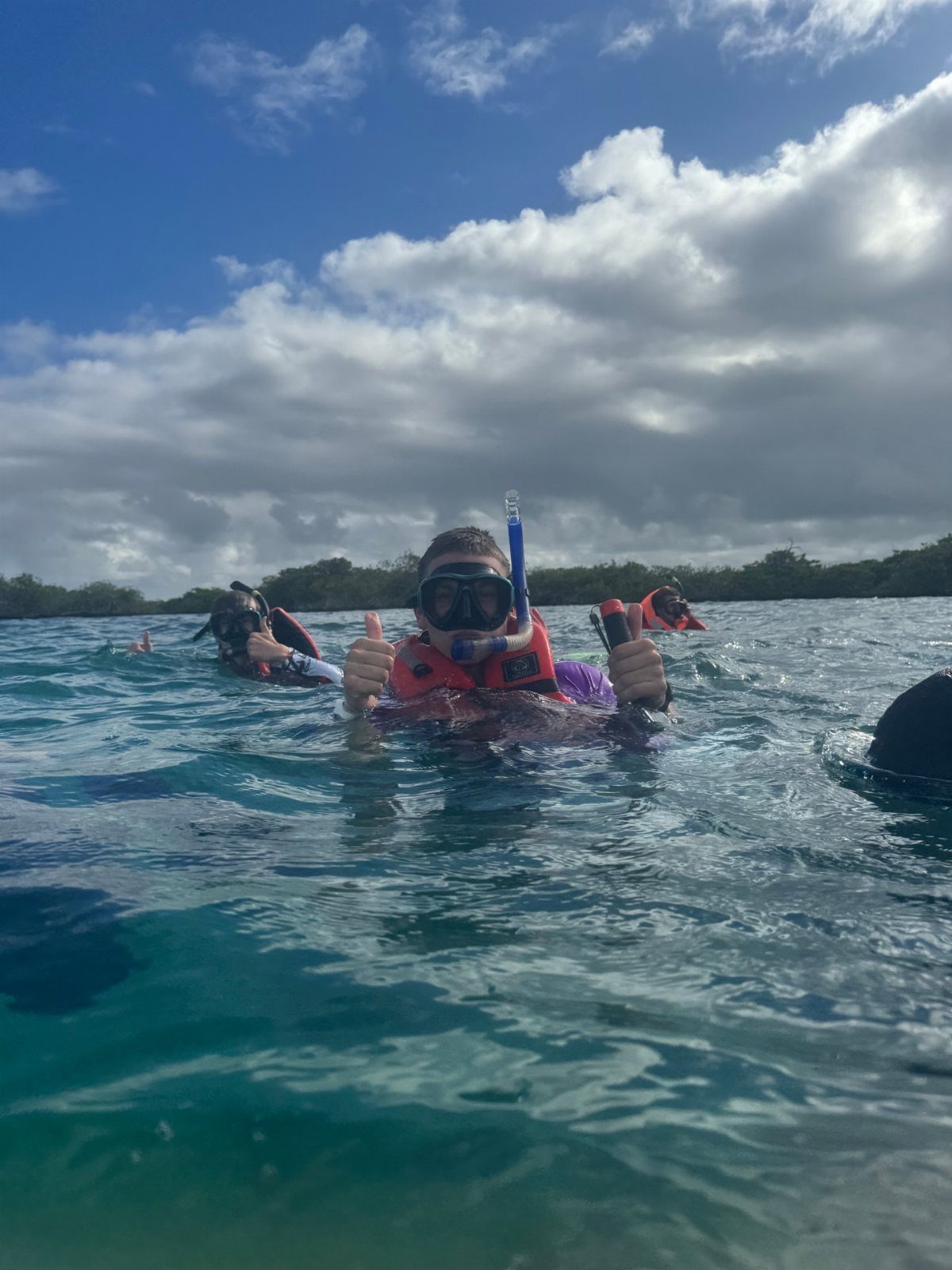 Person in snorkel gear and life vest giving thumbs up in blue ocean water