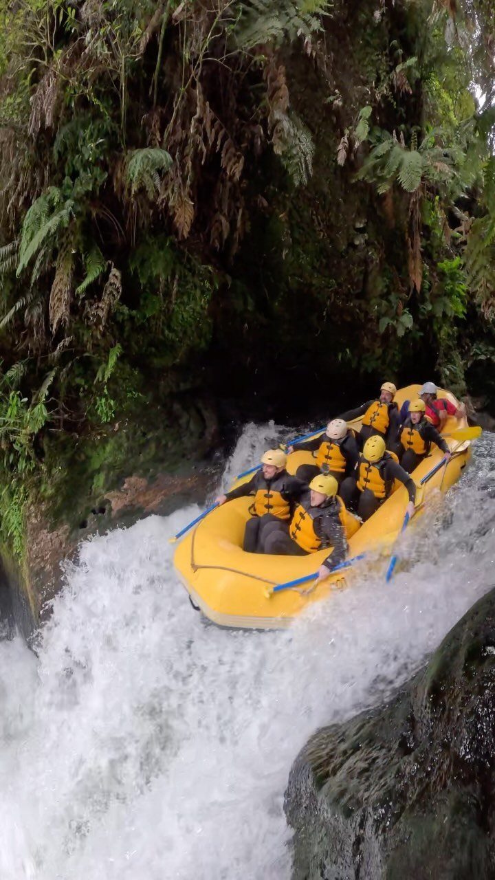 People in a yellow raft navigating white-water rapids through a lush green canyon.
