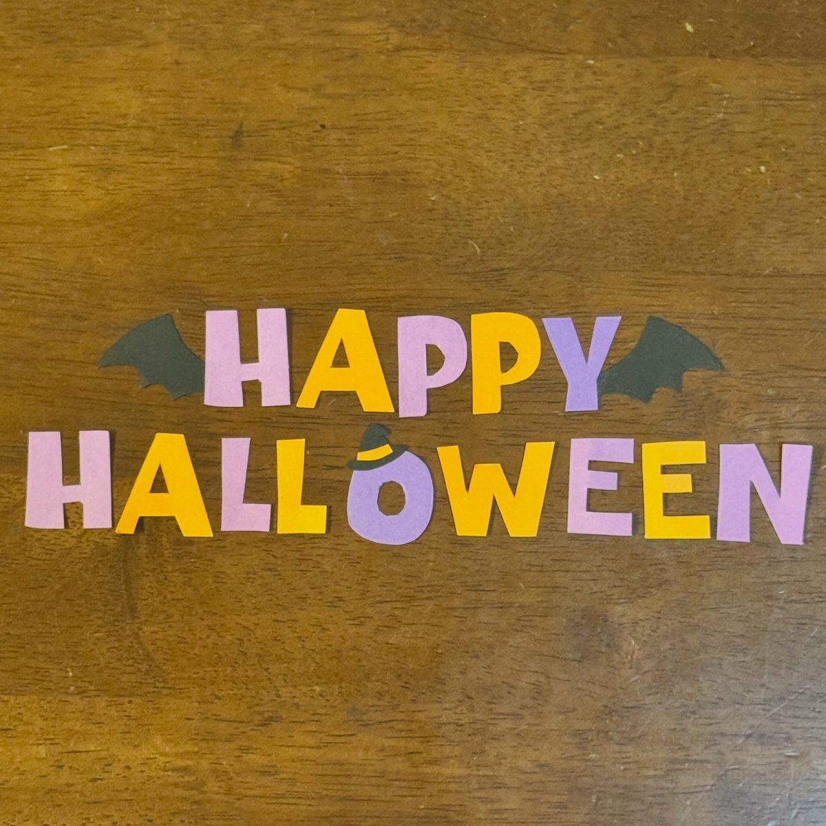 Purple and orange paper letters spelling Happy Halloween on a wooden table.