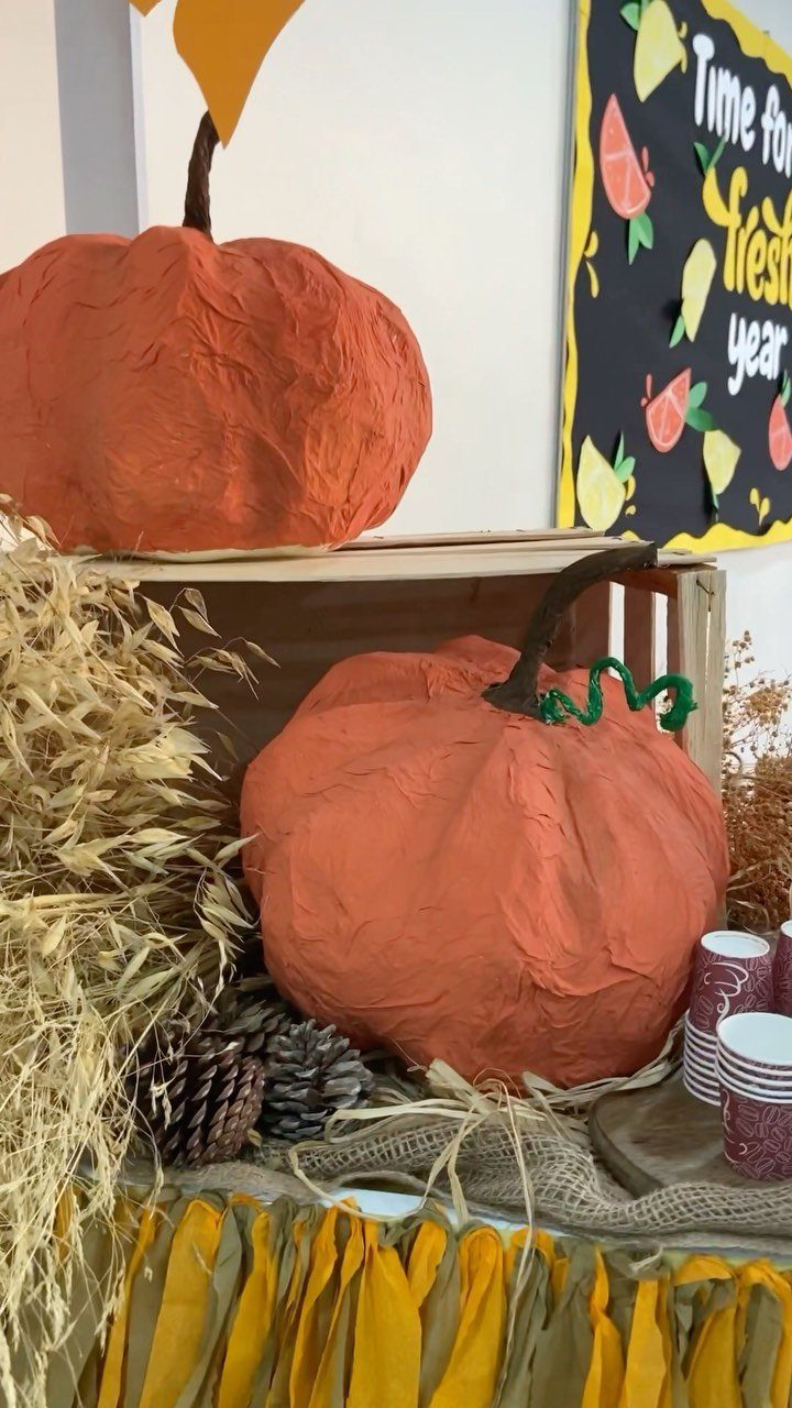 Two orange paper mache pumpkins displayed with dried wheat and pinecones on burlap.