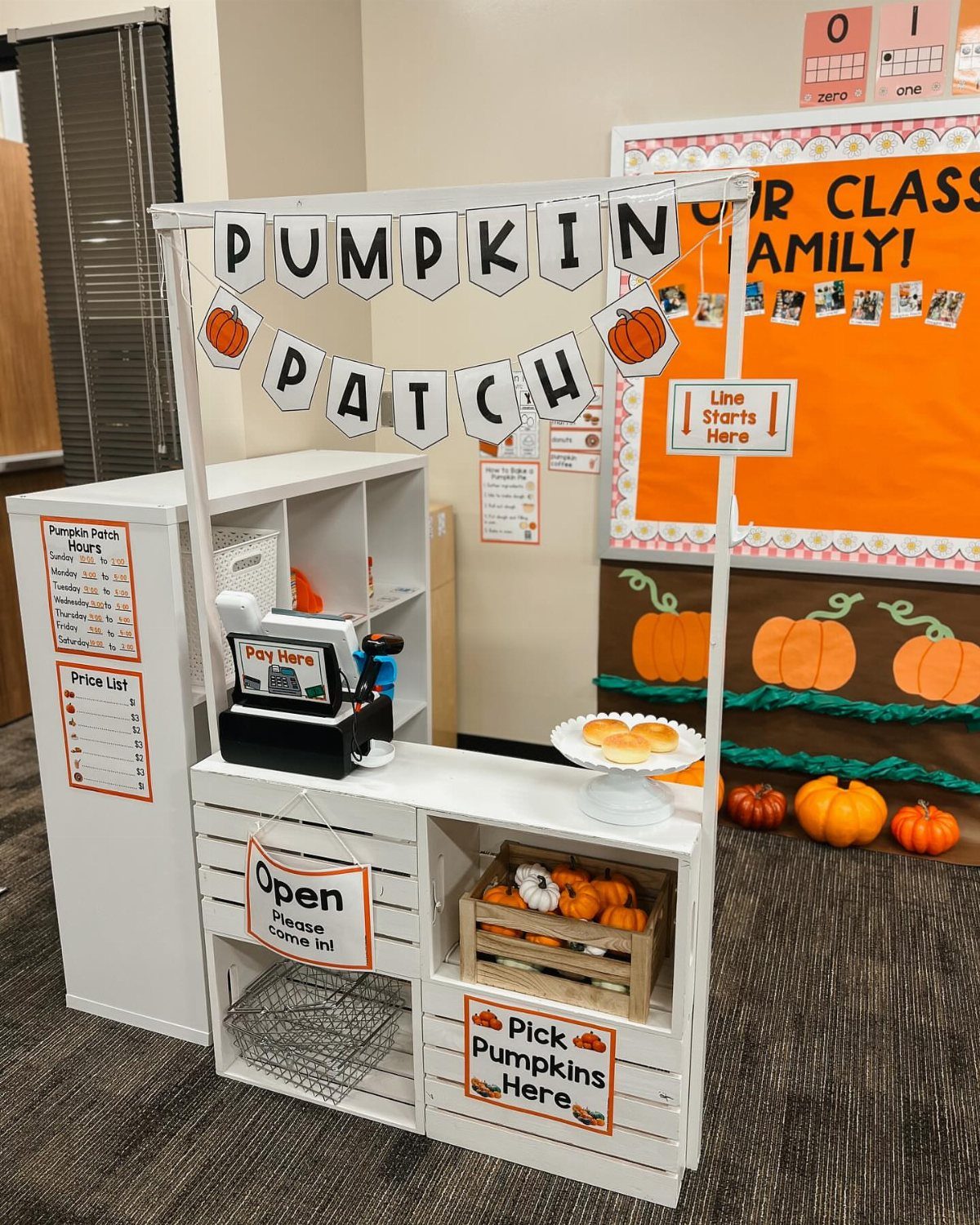 Pumpkin patch classroom display with white stand, toy register, and small pumpkins.